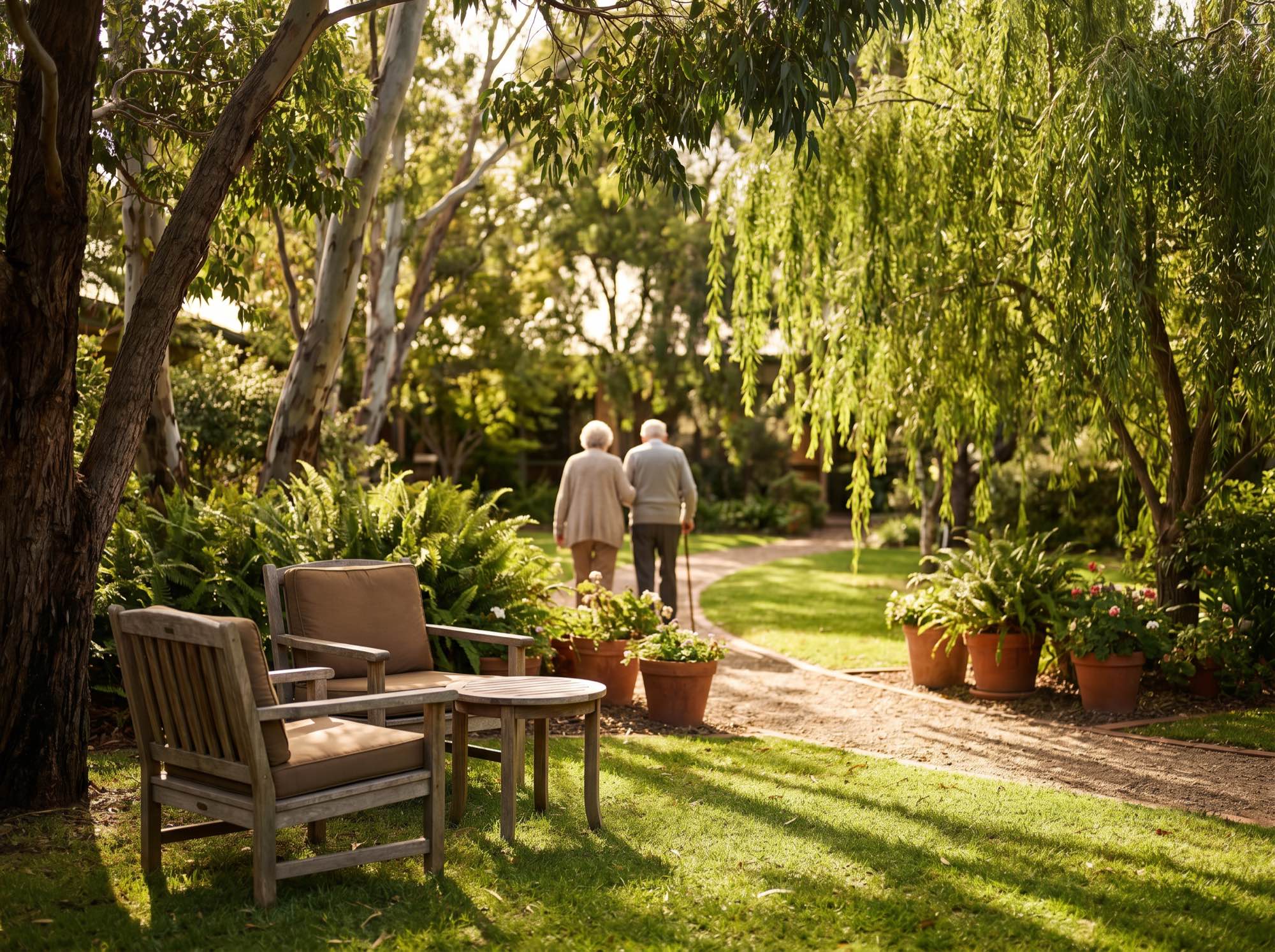 Two residents walking arm in arm along a path through the secure garden in dappled afternoon light.